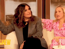 two women sit on a couch in front of a sign that says " crew "