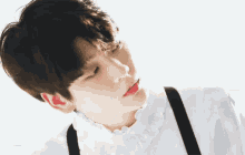 a young boy wearing a white shirt and black suspenders looks down