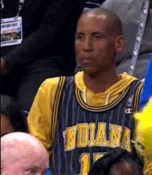 a man wearing a basketball jersey is sitting in the stands at a basketball game .