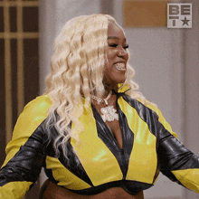 a woman in a yellow and black jacket is smiling in front of a be t logo