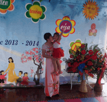 a woman is holding a little girl in front of a sign that says 2013 2014