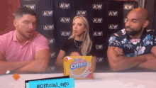 three people are sitting in front of a wall that says aew on it