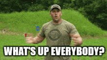 a man in a t-shirt with the words `` what 's up everybody ? '' standing in a field .
