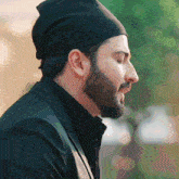 a man with a beard wearing a black hat and a black jacket