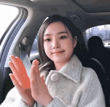 a woman in a white coat is sitting in a car with her hands in the air