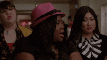 a woman wearing a pink hat with a black band sits with two other women
