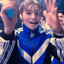 a young man in a blue jacket is waving his hands