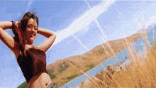 a woman in a crop top stands in a field with a lake in the background