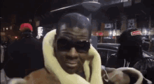 a man wearing sunglasses and a scarf around his neck looks at the camera