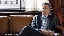a man in a suit and tie is sitting on a couch with the hashtag lawandorder on the bottom