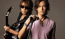 two men are standing next to each other one is holding a guitar and the other is holding a microphone