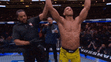 a man in a yellow ufc shorts stands in a cage with his arms in the air