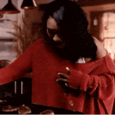 a woman in a red sweater is standing in front of a pan of food .