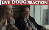 a man in a suit and tie is sitting next to a woman in front of a live doug reaction sign