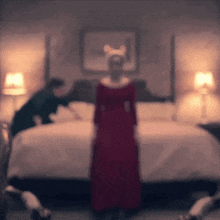a blurry photo of a woman in a red dress standing in front of a bed