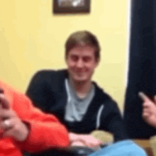 a blurry picture of a man sitting on a couch with a cell phone in his hand .