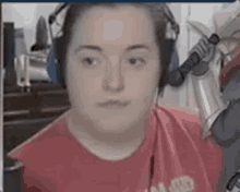 a woman wearing headphones and a red shirt is sitting in front of a computer .