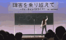 a woman stands in front of a blackboard with the word fuck written on it
