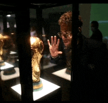 a man with curly hair and glasses looks at a trophy in a glass case