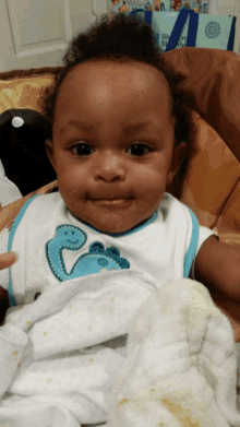 a baby wearing a bib with a dinosaur on it is sitting in a high chair