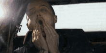 a man with a tattoo on his arm is yawning while sitting in a car