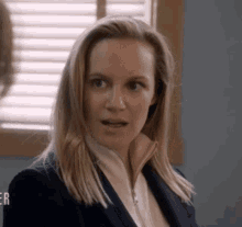 a woman in a suit is sitting in front of a window and making a surprised face .
