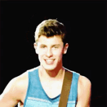 a young man wearing a blue tank top is playing a guitar