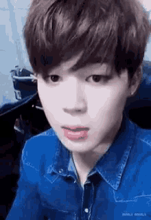 a close up of a young man wearing a blue denim shirt making a funny face .