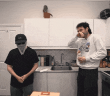 two men are standing in a kitchen with one wearing a bandana