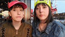 a woman wearing a pink hat and a green hat is making a face next to another woman wearing a denim jacket .