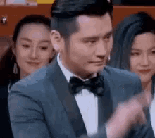 a man in a suit and bow tie is clapping his hands while sitting in a theatre .