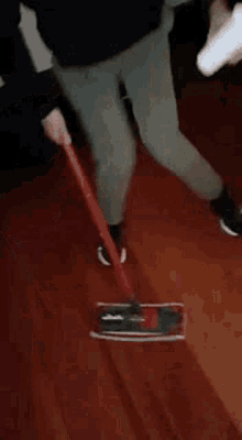 a man is standing on a wooden floor holding a mop .