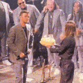 a group of people are standing around a woman holding a cake