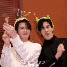 two men wearing party hats are standing next to each other in front of a wall with the words beatxl below them