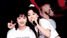two women are standing next to each other and one is holding a microphone and the other is giving a peace sign