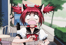 a girl with red hair and cat ears is sitting at a table