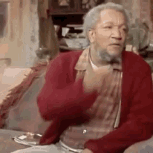 an elderly man with a beard is sitting on a couch wearing a red sweater .