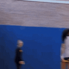 a blurry photo of a person walking in front of a blue wall