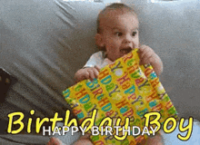 a baby is sitting on a bed holding a birthday present and says happy birthday