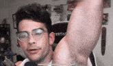 a man wearing glasses shows off his armpit in front of a ferrag chair