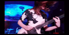 a woman in a tie dye shirt is playing a guitar on stage
