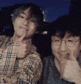 a man in a plaid shirt giving a thumbs up next to another man wearing glasses