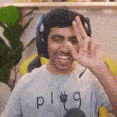 a man wearing headphones and a plug t-shirt is smiling and giving the ok sign .