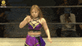 a woman in a purple outfit is standing in a wrestling ring with a man taking a picture behind her