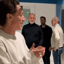 a group of men are standing in a room and one of them is talking