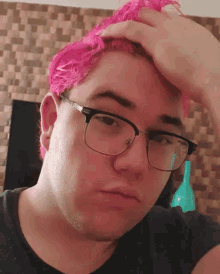 a young man with pink hair and glasses holds his hand to his forehead
