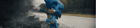 sonic the hedgehog is standing on the side of a road in front of a burning car .