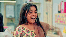 a young girl is laughing with her mouth open and wearing a floral top .