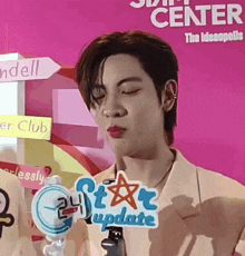 a young man with his eyes closed is standing in front of a pink wall holding a microphone .