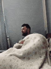 a man with a beard is laying under a blanket
